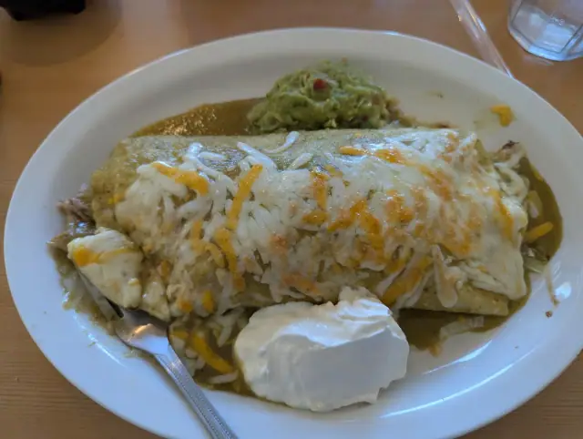 A big burrito covered in green sauce and melted cheese with a scoop of sour cream